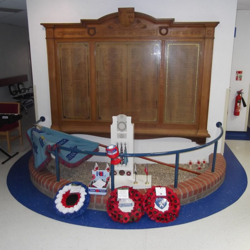 Photo showing the War Memorial with a flag and three poppy wreaths laid in front