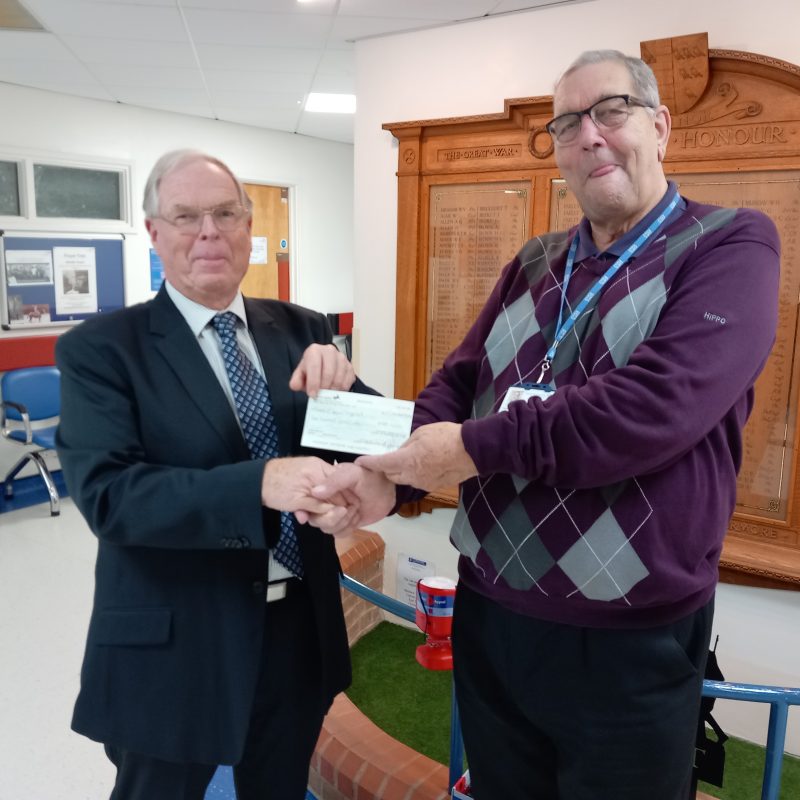 Stephen Hymes presents a cheque to Chairman Brian Knight while standing in front of the War Memorial