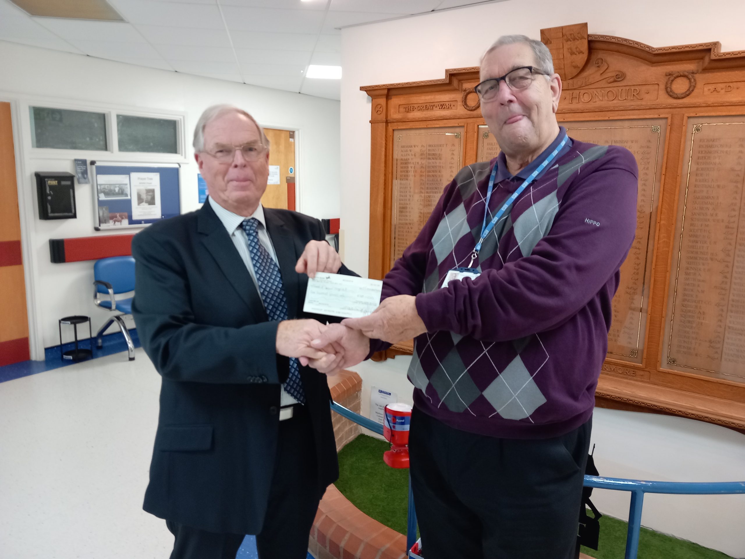 Stephen Hymes presents a cheque to Chairman Brian Knight while standing in front of the War Memorial