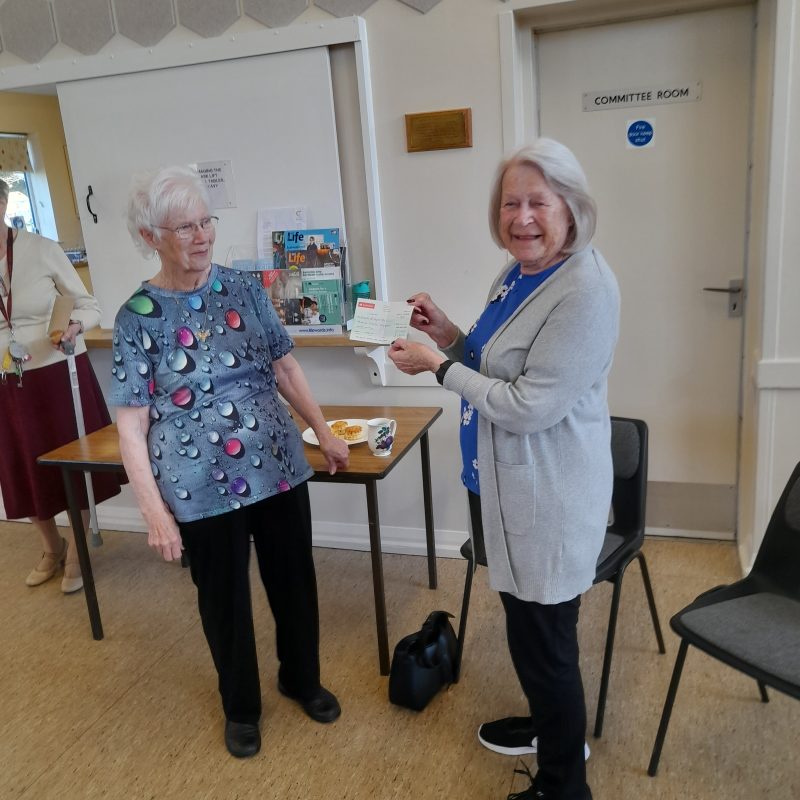 June a Trustee of the Friends is smiling widely as she receives a cheque from a representative of the West Meads coffee morning