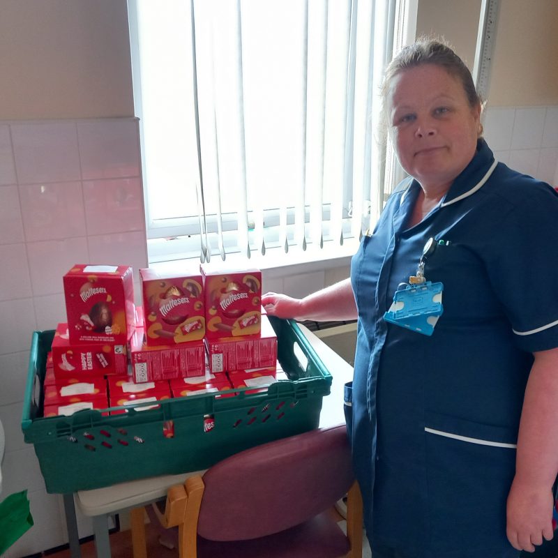 Nurse dressed in blue stands with a large tray of red easter eggs