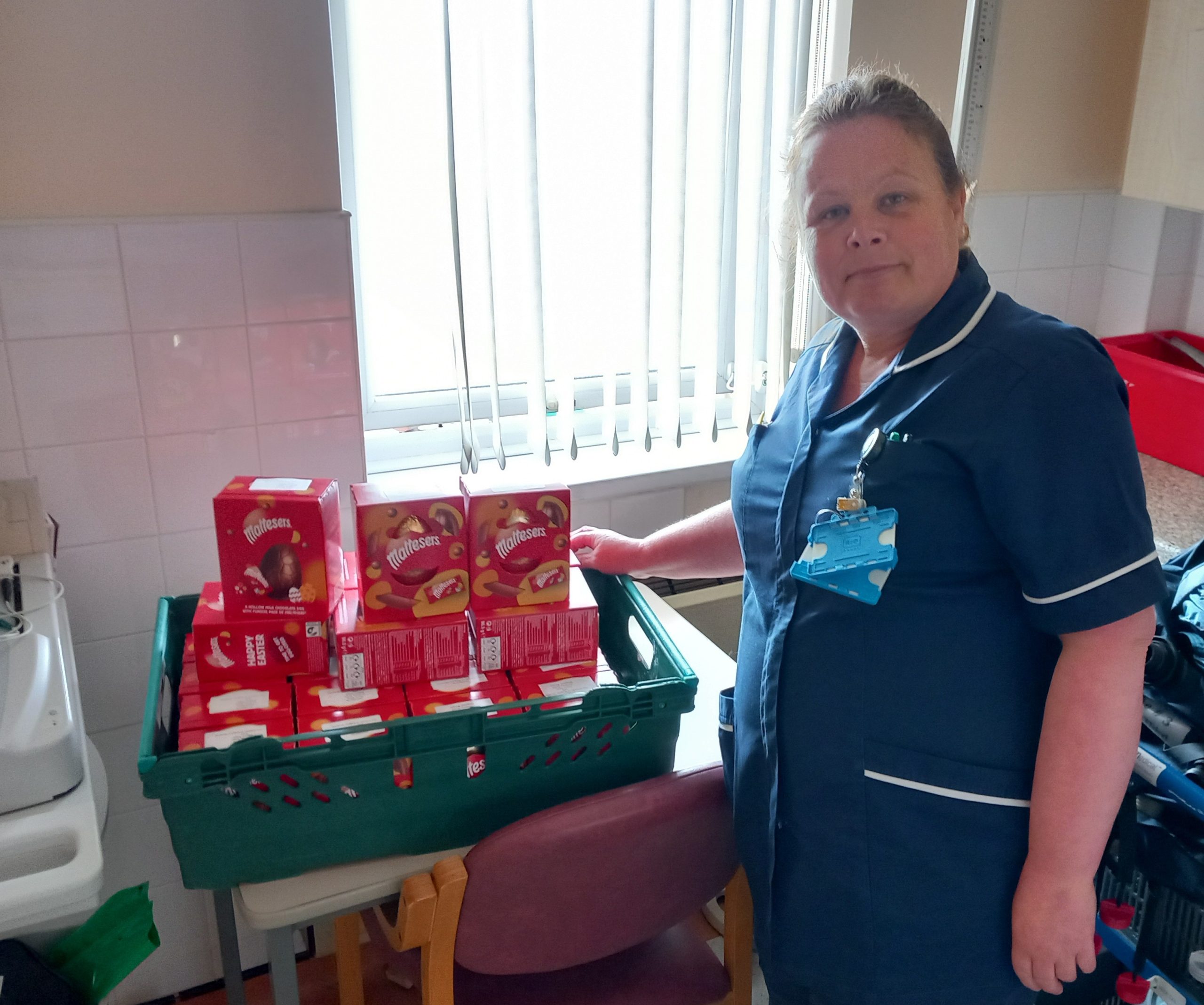 Nurse dressed in blue stands with a large tray of red easter eggs
