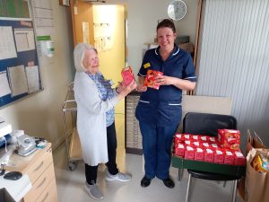 Nurse dressed in blue receiving a read Easter Egg from June a Trustee