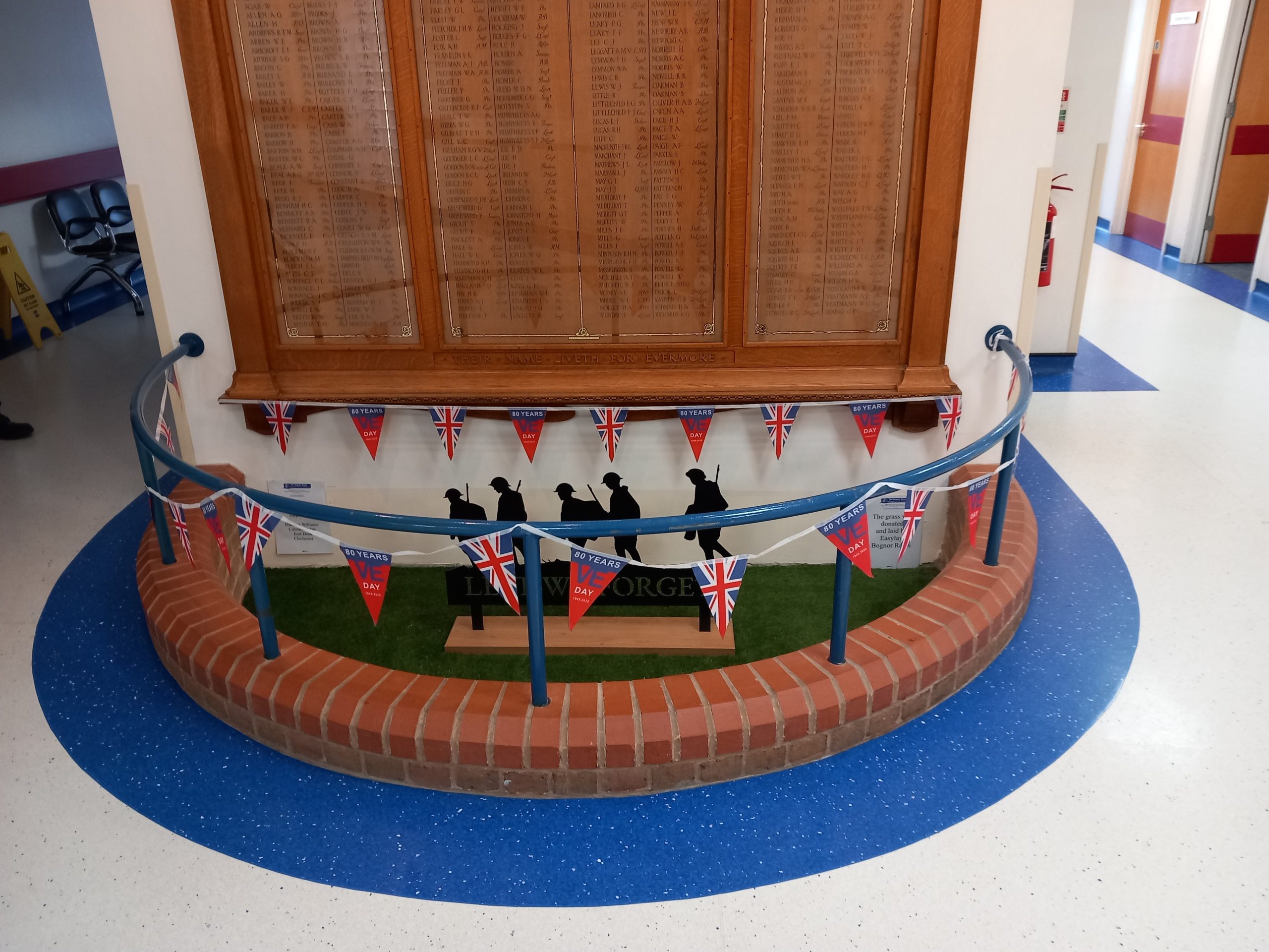 The War Memorial Roll of Honour is pictured with black silhouetted military figures in front, and the Memorial is string with union flag bunting