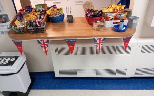The Friends Tea Bar counter is pictures with lots of goodies for sale in baskets and union flag bunting fixed across