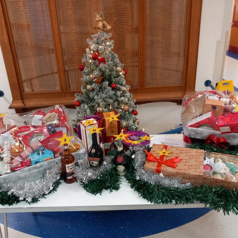 Table in front of the War Memorial which is laid with a small decorated Christmas tree, three wrapped hampers full of goodies, plus spirits and chocolate prizes.